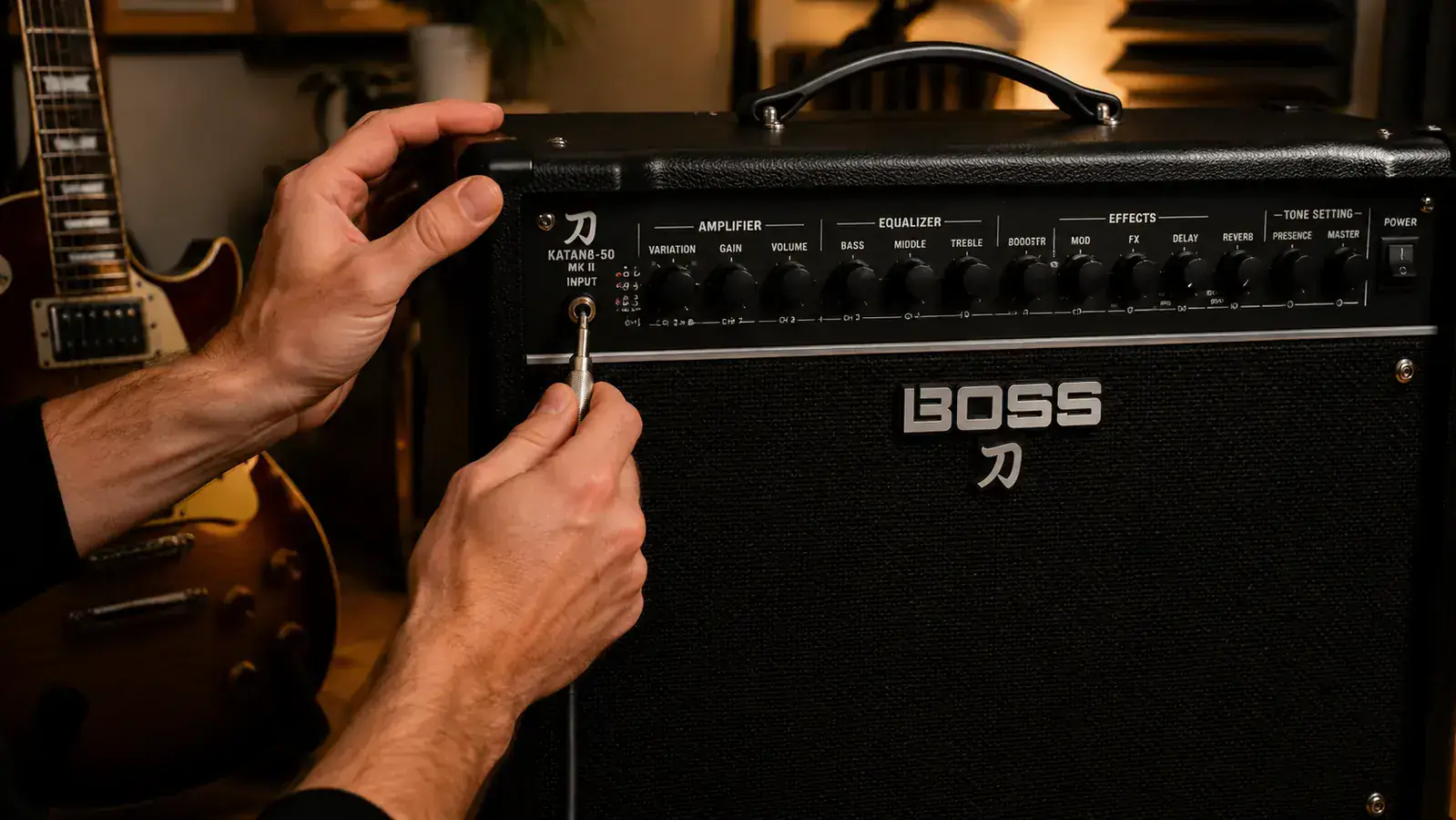 Guitarist plugging a Les Paul into the Boss Katana MkII-50 input jack, close-up of hands and amp panel