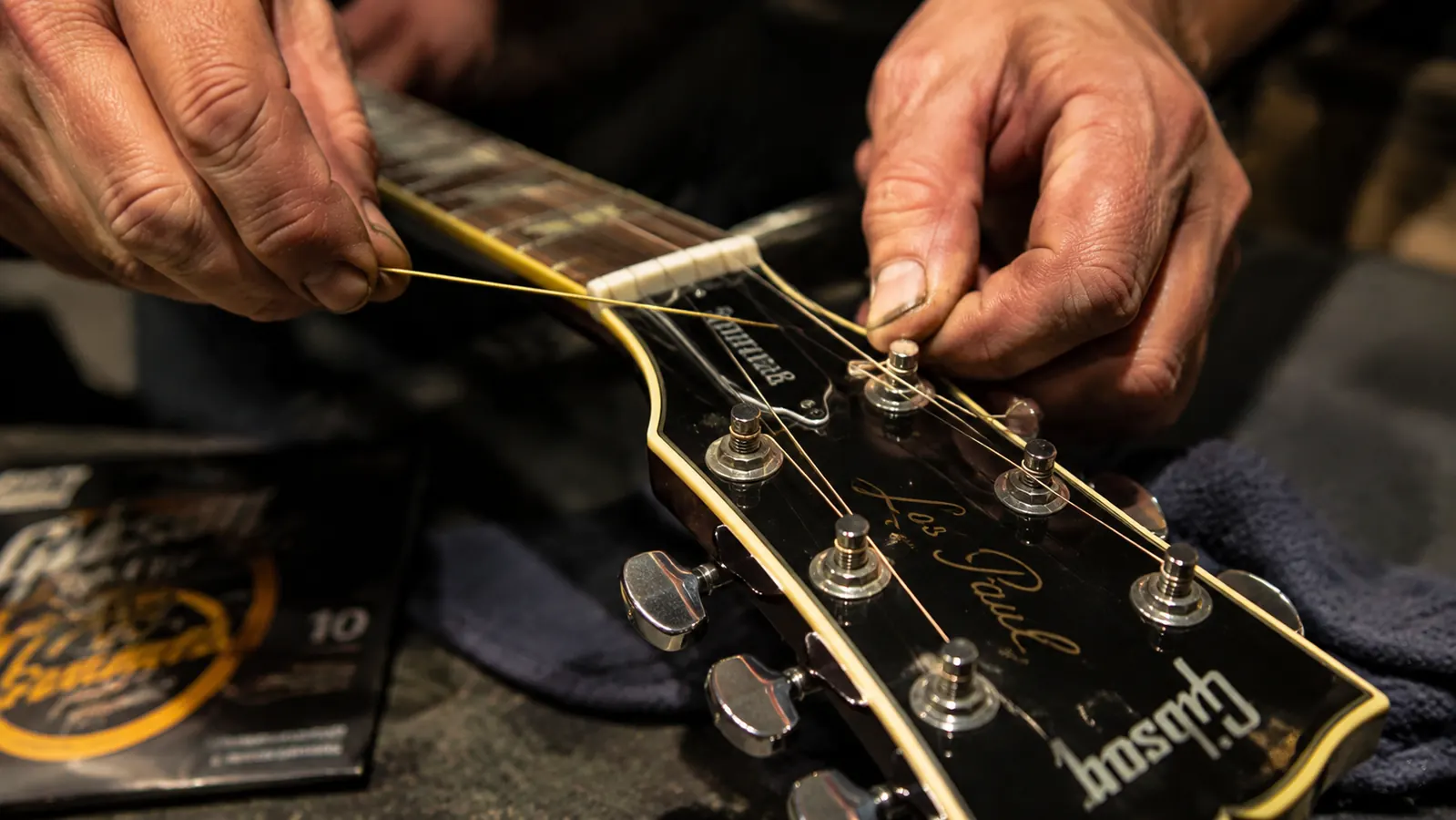 Guitarist pulling a string upward with two fingers to stretch it in after a fresh restring
